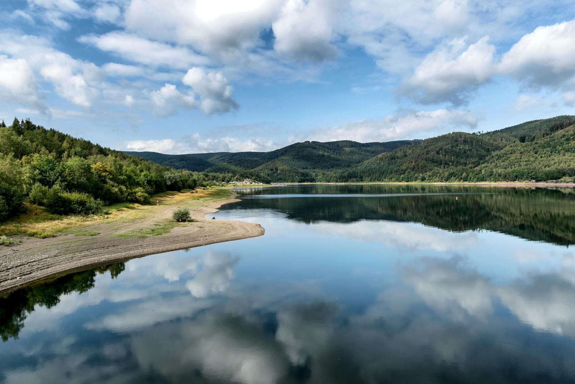 Serene summer view of a tranquil lake reflecting fluffy clouds in Harz, Germany.