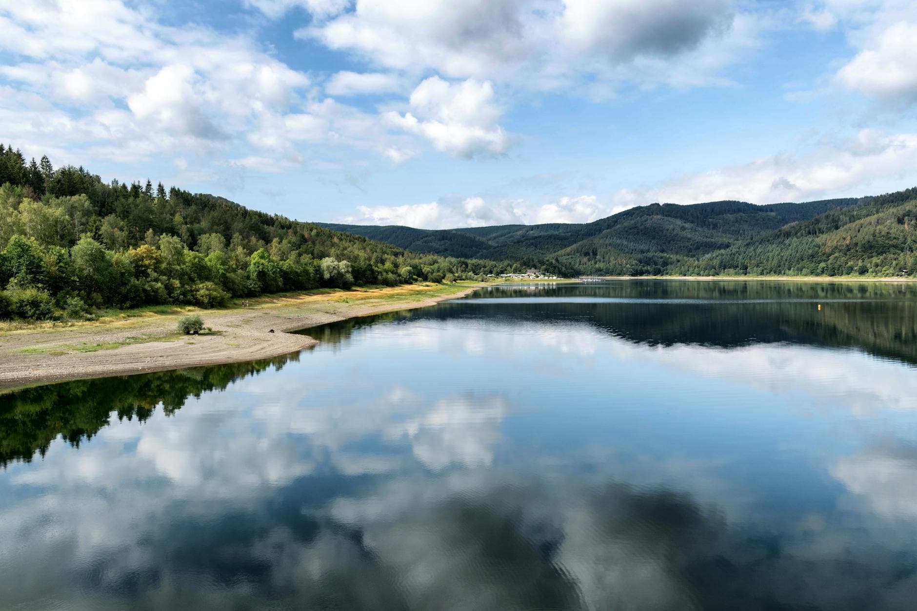 Tranquil lake with forested hills and sky reflections in Langelsheim, Germany.